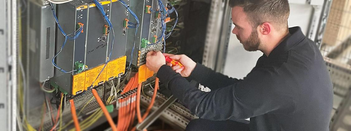 echnician working on electrical modules and wiring inside an industrial cabinet.