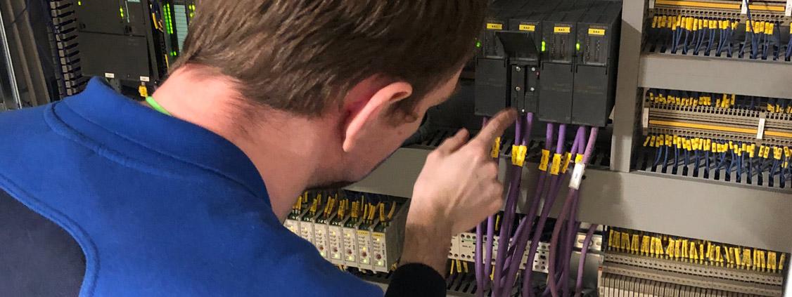 UNIS Group employee inspecting and documenting industrial control equipment inside an electrical cabinet.