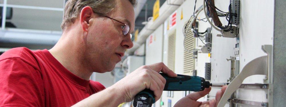 Technician using a cordless screwdriver to service industrial electrical equipment inside a machine cabinet.