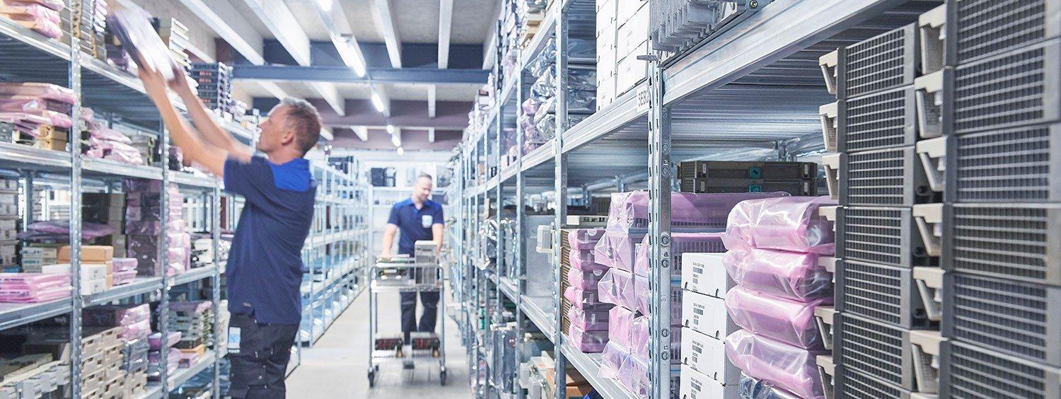 Warehouse employees organizing packaged equipment on storage shelves.
