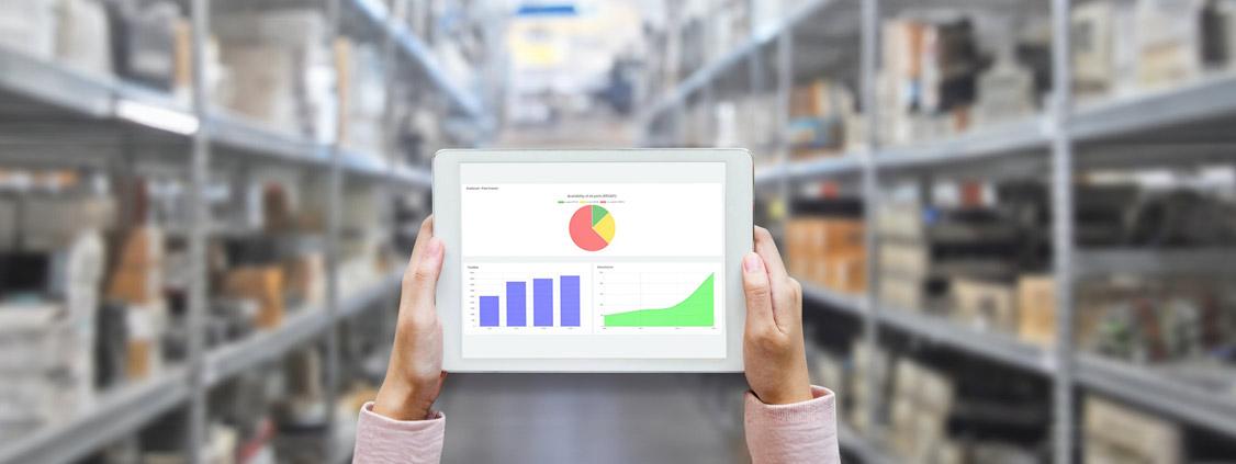 Person holding a tablet displaying inventory charts in a warehouse aisle.