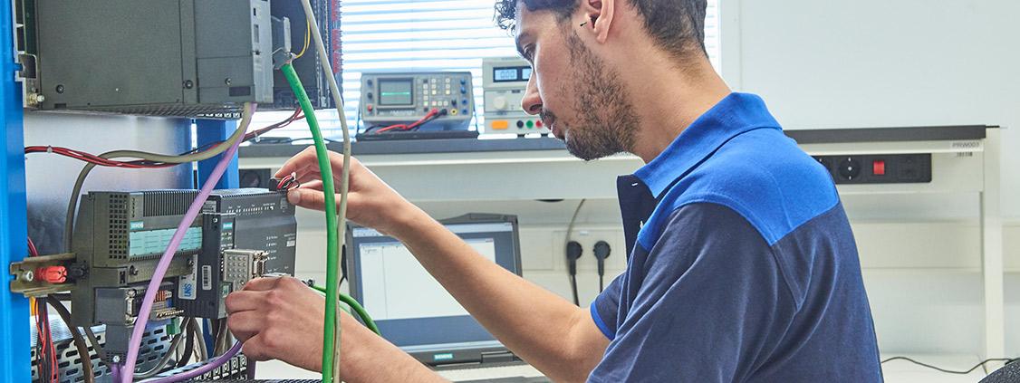 Technician inspecting and testing industrial electronic equipment connected to diagnostic instruments.