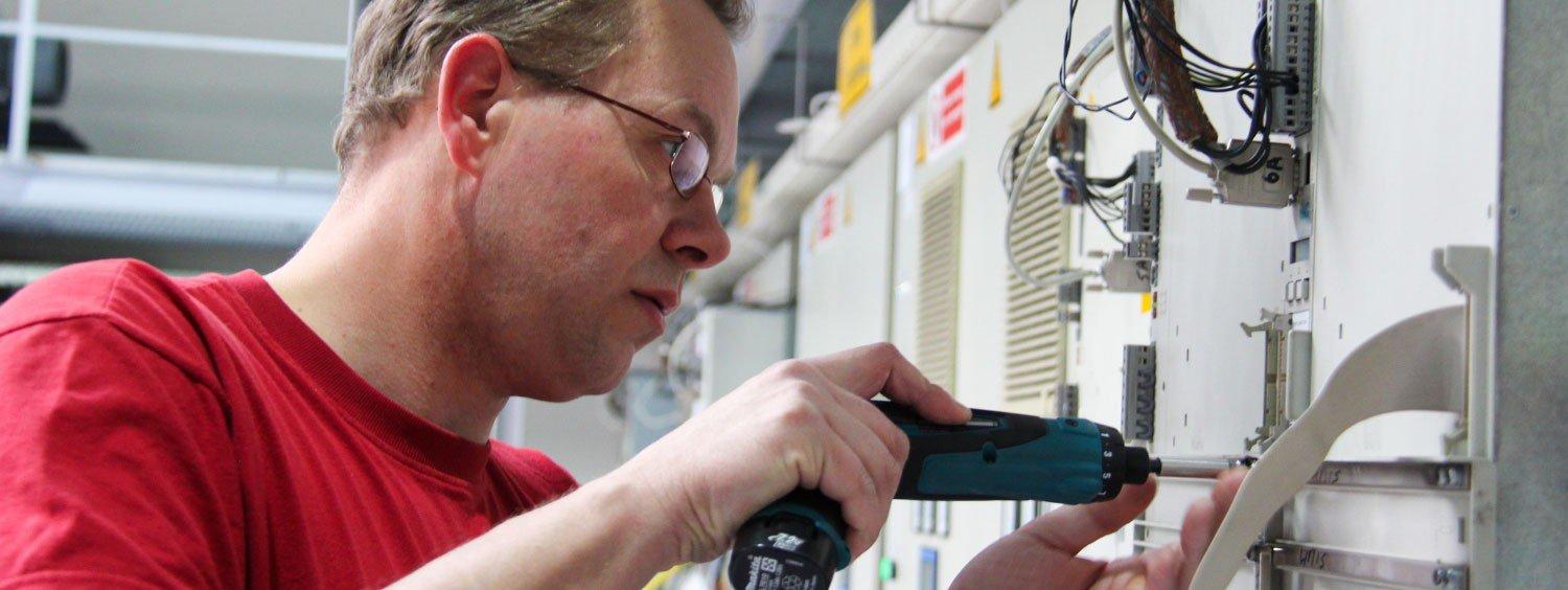 Technician using a cordless screwdriver to service industrial electrical equipment inside a machine cabinet.